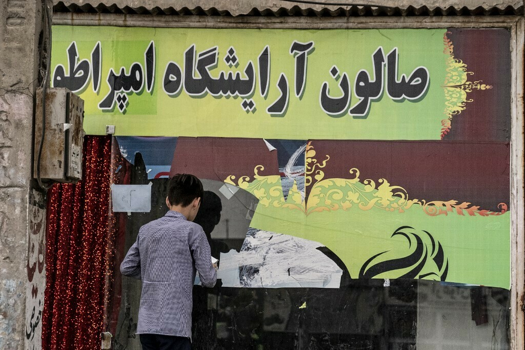  An afghan boy peels off stickers from a window of closed beauty parlour in Kabul on July 25, 2023. Photo: AFP 