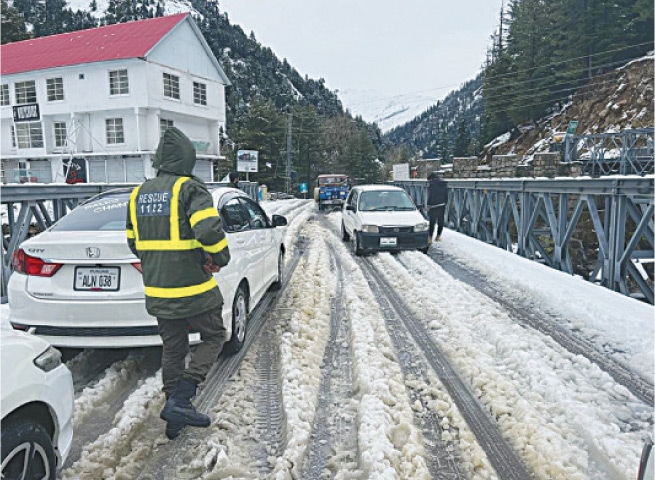 A Rescue 1122 official walks on a snow-covered bridge in Naran to assist motorists. — Dawn