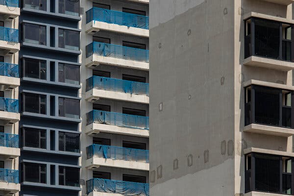 A close-up view of the windows and terraces of several apartment towers under construction. The terraces are covered with a sheer blue material.