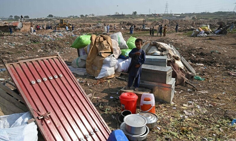 An Afghan refugee boy stands along with his belongings after local authorities demolished his house, at a refugee camp in Islamabad on October 31. — AFP