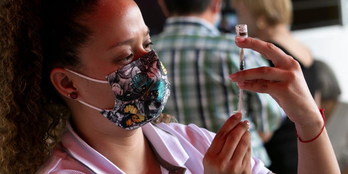 A nurse wearing a flowered mask and a pink shirt measures out a dose of COVID-19 vaccine on May 7, 2021 in Escazu, Costa Rica, as two people are blurry in the background