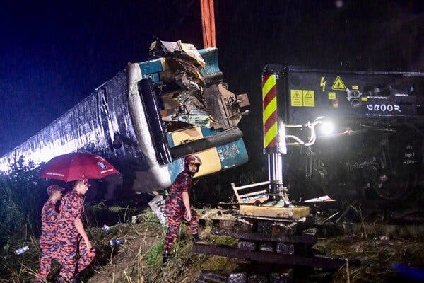 An overturned train car at night. Three people in brightly colored uniforms head toward the train.