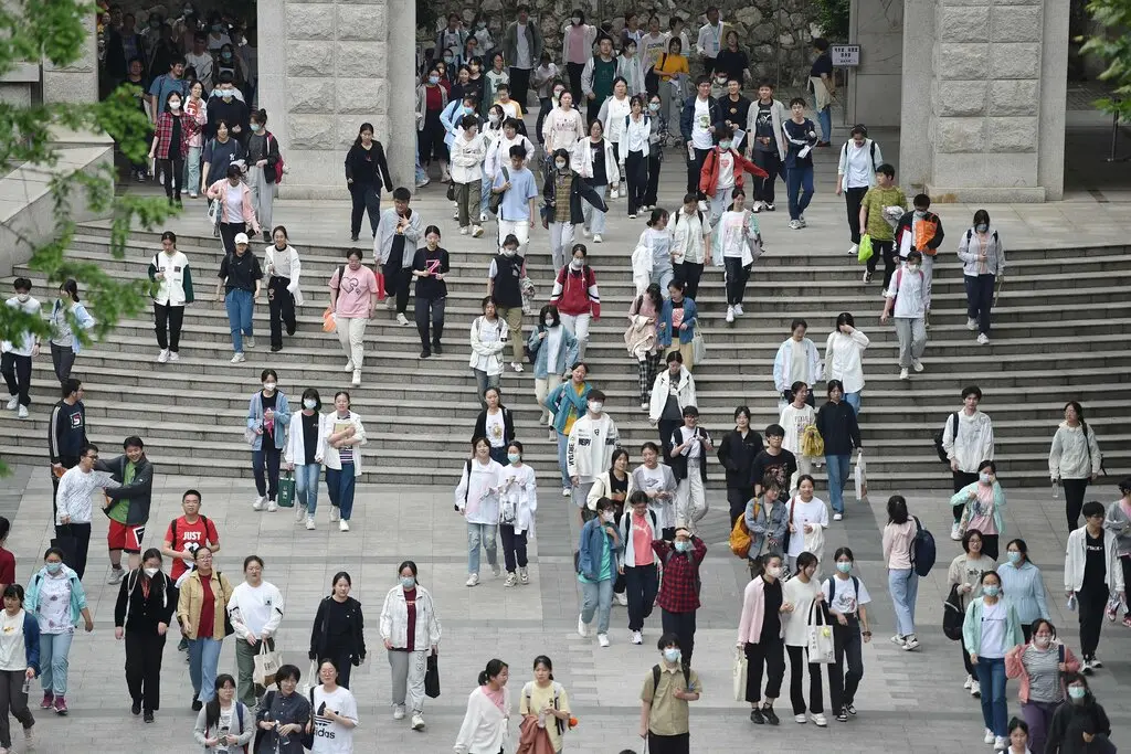 A large crowd of students, some walking down steps, walk on a building’s plaza after taking a college-entrance exam. 
