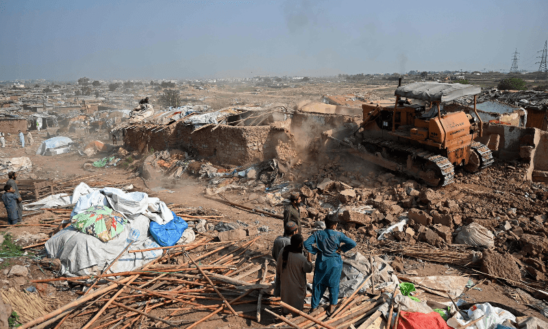  A bulldozer is being used to demolish houses of Afghan refugees, during an operation by local authorities at a refugee camp in Islamabad on October 31. — AFP 