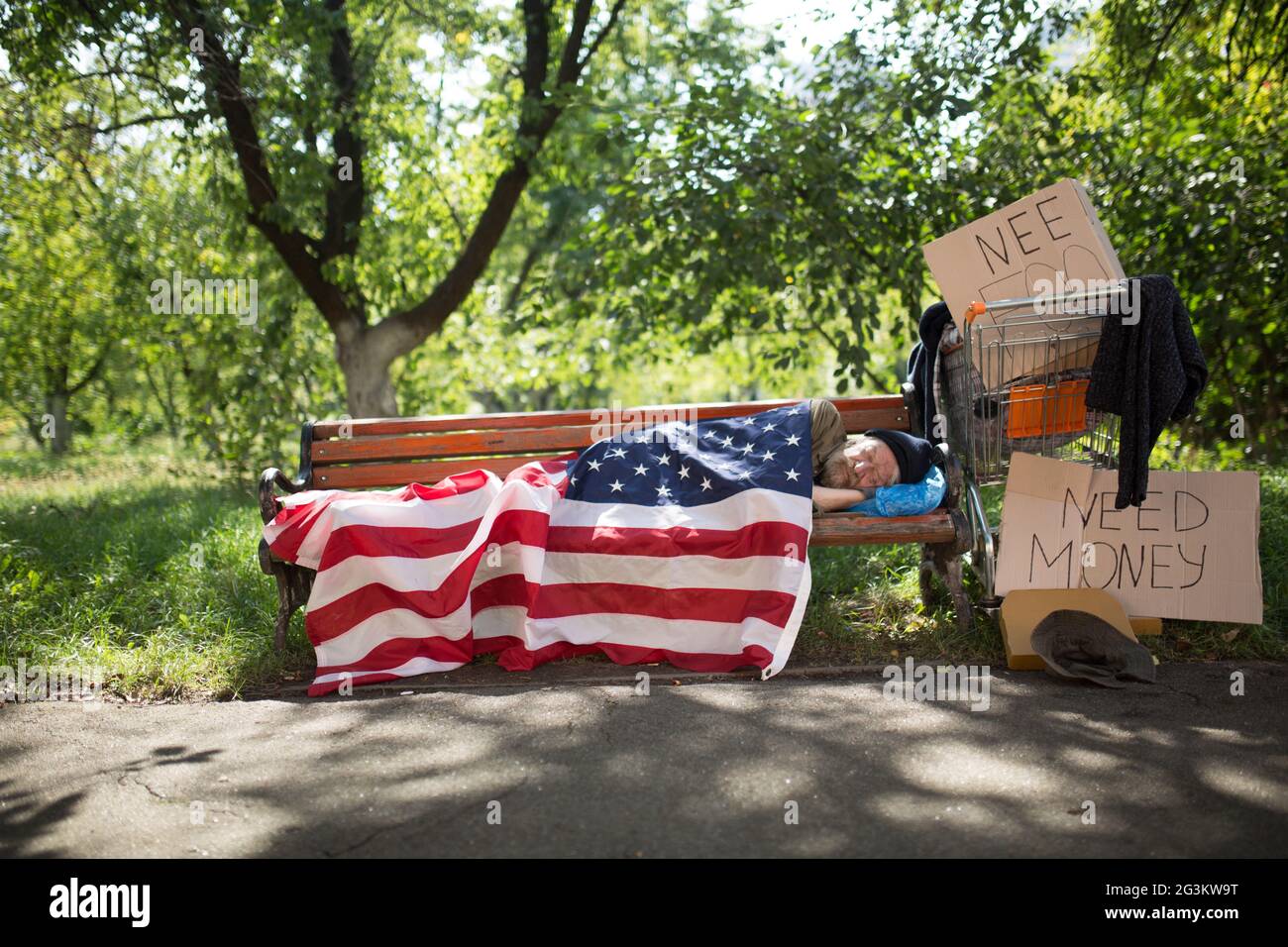 view-of-a-homeless-man-lying-on-bench-covered-with-usa-flag-2G3KW9T.jpg