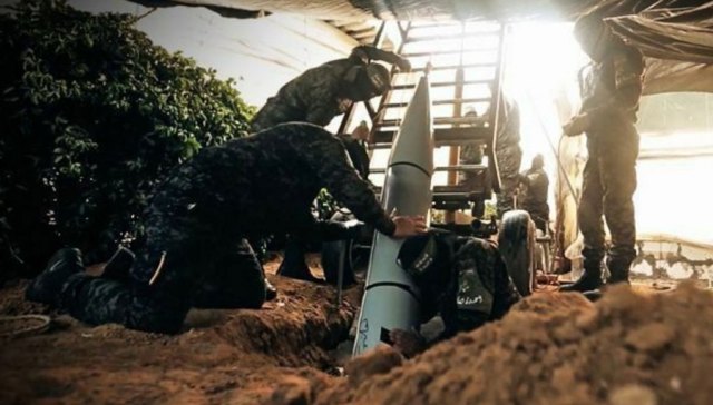 Hamas fighters loading a heavy rocket in an underground silo under camouflage