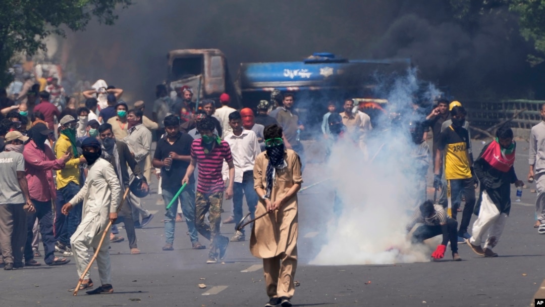 FILE - Supporters of Pakistan's former Prime Minister Imran Khan remove tear gas shell fired by police to disperse them during a protest in Lahore, Pakistan, May 10, 2023.