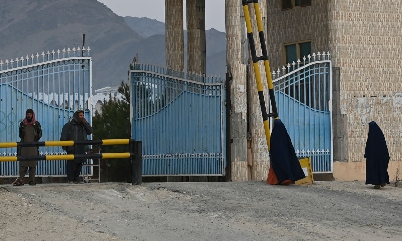 Women wearing a burqa walk toward the main gate of Laghman University as Taliban fighters stand guard in Laghman province, Afghanistan, February 2. — AFP