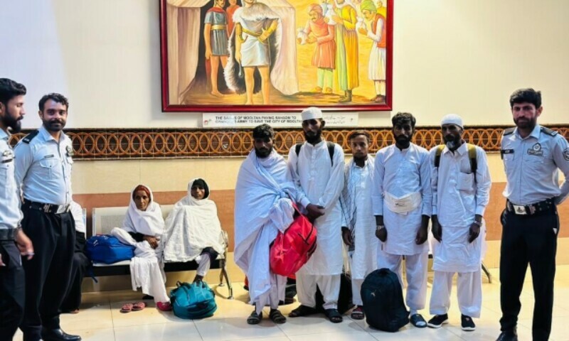 Beggars offloaded from a Saudi Arabia-bound flight pose for a photograph with FIA officials at the Multan airport. — Dawn/ImranGabol