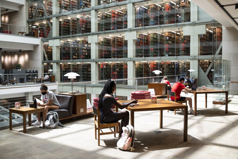 Students wearing protective masks study at desks inside a library