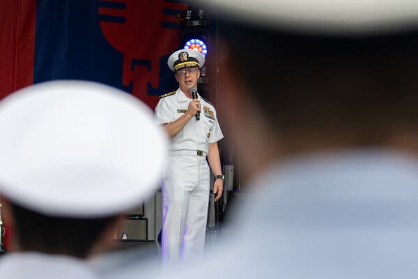Adm. Daryl Caudle speaking to sailors with a microphone on a stage. 