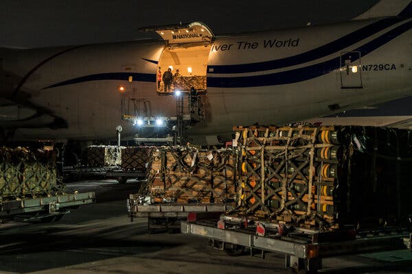 Pallets full of missiles and weapons being unloaded from an airplane at night.
