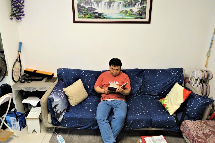 Cheng Shi sits and reads on a couch in his condo. 