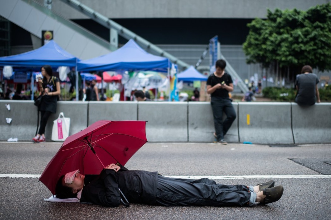 A protester rested on a blockaded road Saturday, shielding himself with an umbrella.jpg