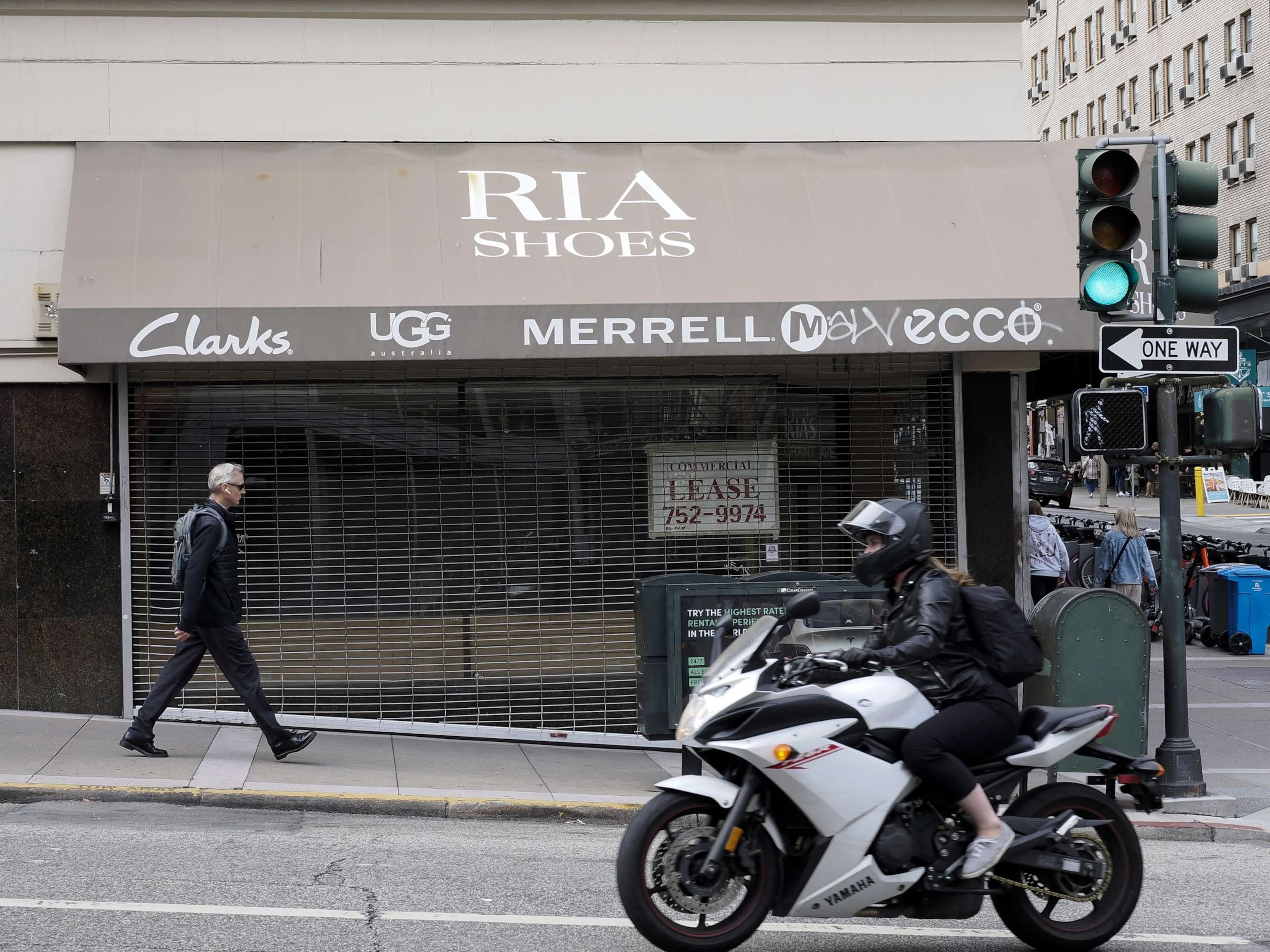 PHOTO: A pedestrian and motorcyclist pass by a closed footwear store in San Francisco, Calif., on July 6, 2023.