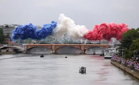 Lars Baron/Getty Images Smoke resembling the flag of Team France is shown over Pont d’Austerlitz during the opening ceremony of the Olympic Games Paris 2024 on July 26, 2024 in Paris, France
