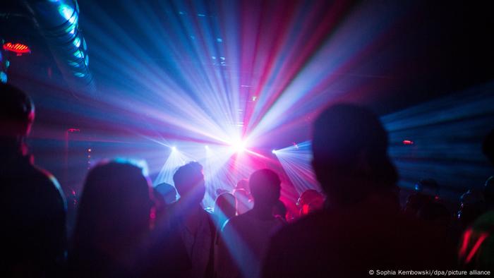 Clubbers dance in a darkened dance club with blue and purple lights