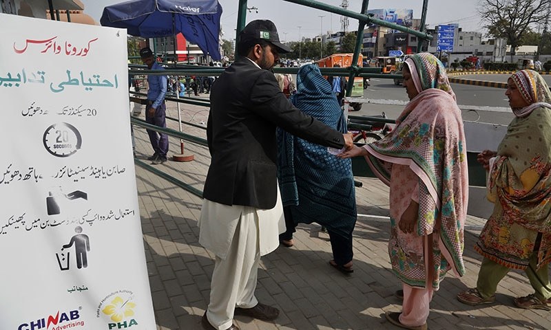 A worker provides sanitizer to visitors outside a park next to a banner informing precautions about the coronavirus in Lahore. — AP/File