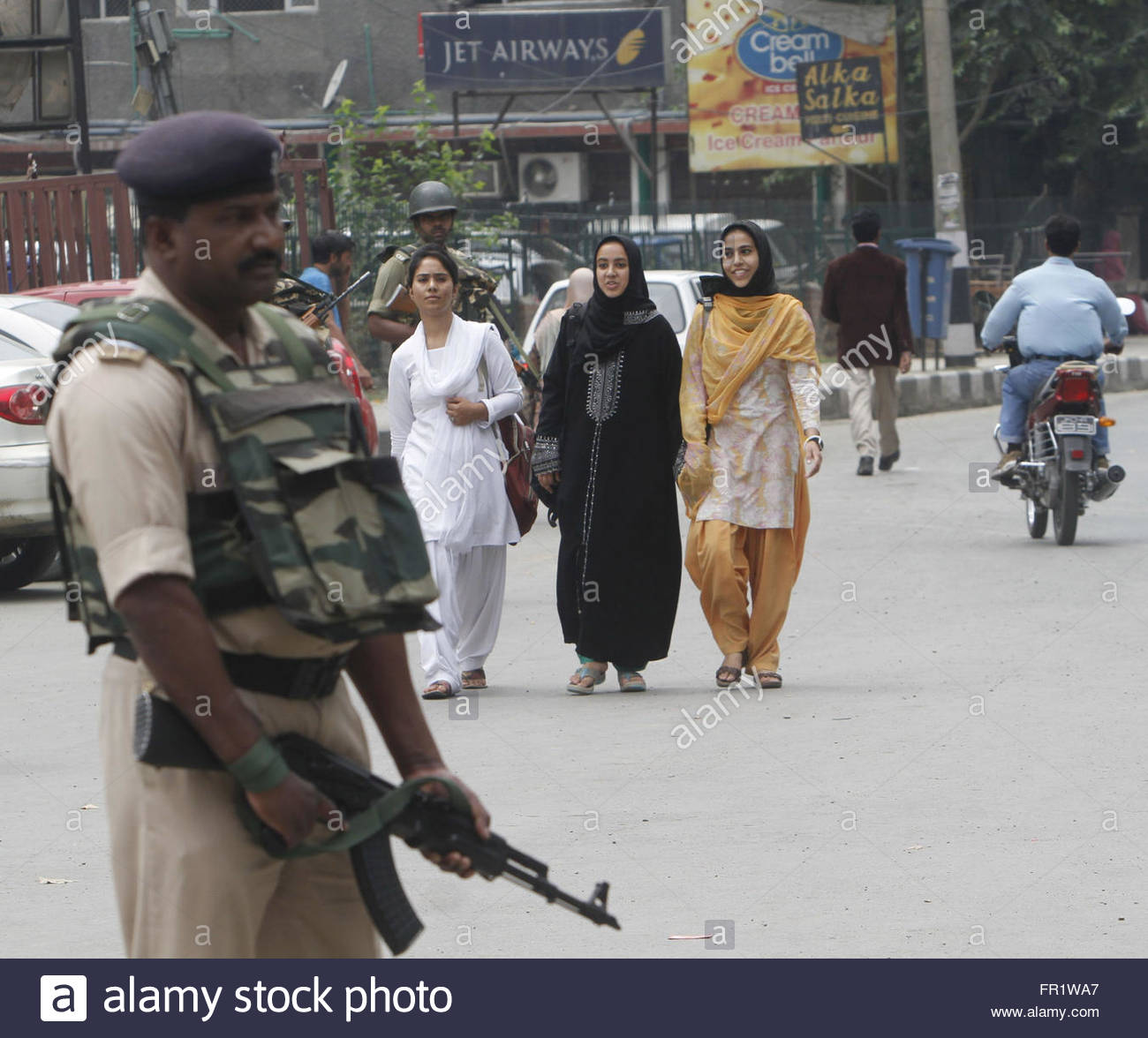 an-indian-paramilitary-solider-stands-guard-as-kashmiri-girls-walk-FR1WA7.jpg