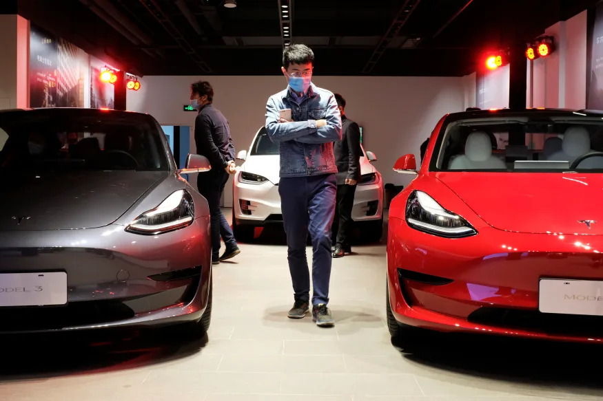 A man wearing a face mask following the coronavirus disease (COVID-19) outbreak walks by Tesla Model 3 sedans and Tesla Model X sport utility vehicle at a new Tesla showroom in Shanghai, China May 8, 2020. Picture taken May 8, 2020. REUTERS/Yilei Sun