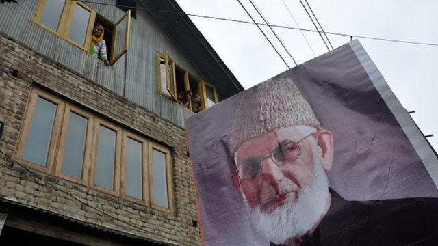 Kashmiri Muslim women look from the windows of there house as a poster of senior separatist leader Syed Ali Shah Geelani is carried by the people during a pro freedom demonstration in Srinagar.