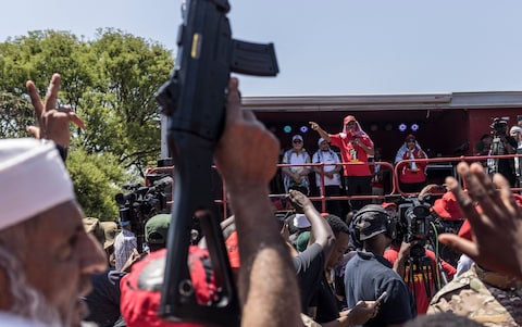 Mr Malema on stage as a man brandishes a replica toy gun during a pro-Palestinian demonstration in front of the Israeli embassy in Pretoria