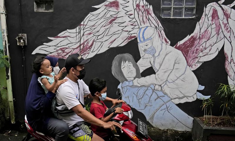 A family wearing masks to help curb the spread of coronavirus outbreak rides on a motorcycle past a Covid-19-related mural in Jakarta, Indonesia. — AP