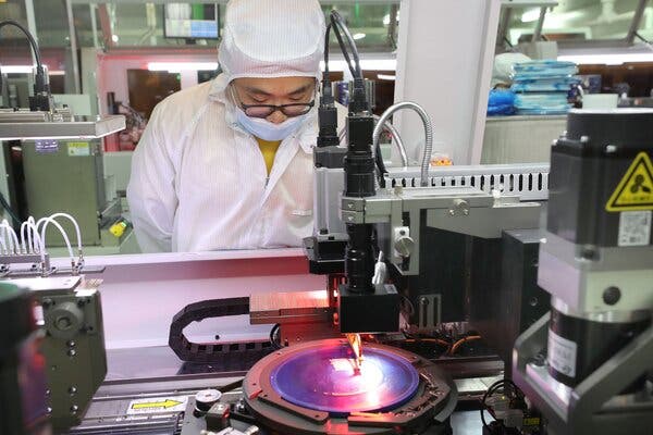 A worker in a white shirt and hat looking down at a machine making semiconductor chips.