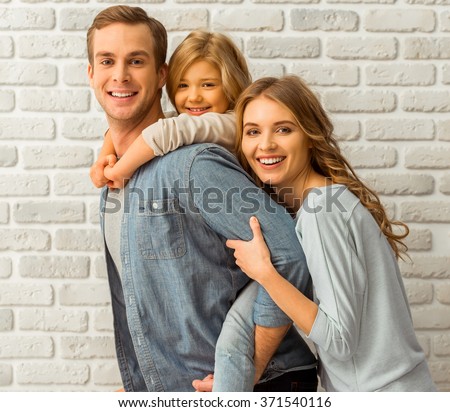 stock-photo-beautiful-young-family-hugging-looking-in-camera-and-smiling-while-standing-against-white-brick-371540116.jpg