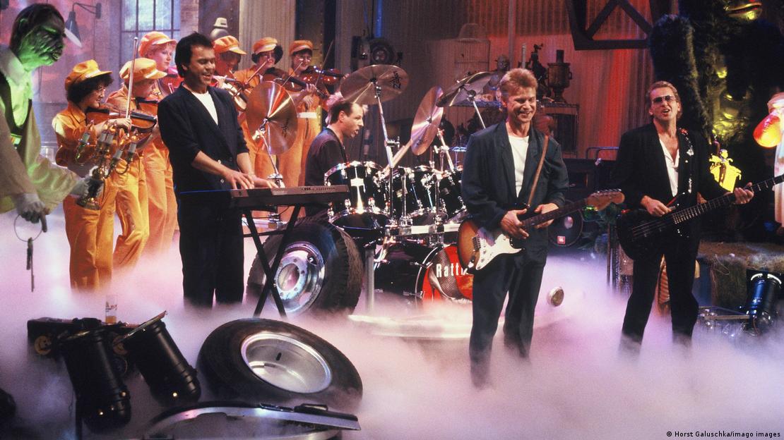 Band performing amid tires and fog on a TV set.