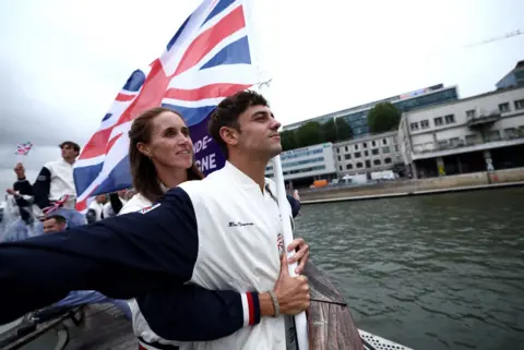 Naomi Baker/Reuters  Flagbearers Tom Daley and Helen Glover, of Team GB, gesture on a boat while holding the national flag on the River Seine during the opening ceremony