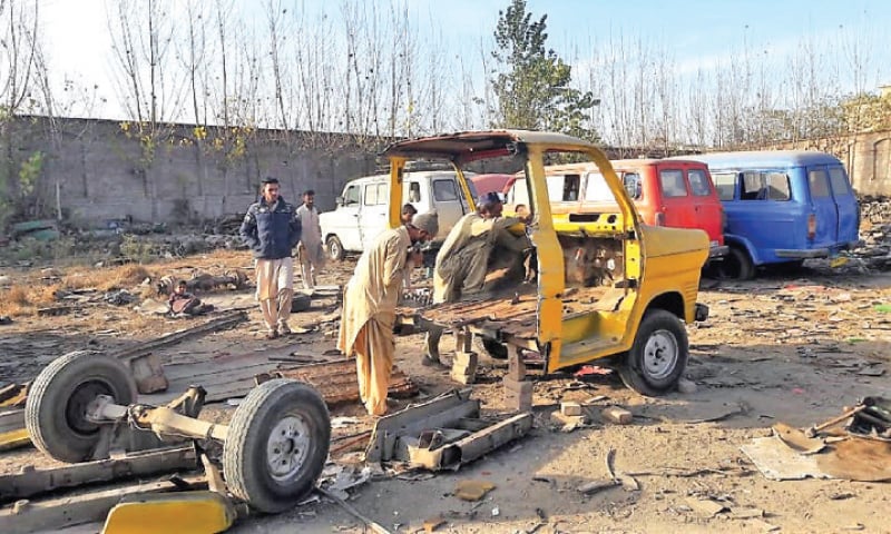 Mechanics work on the chassis of a Ford van at a workshop in Peshawar. — Dawn