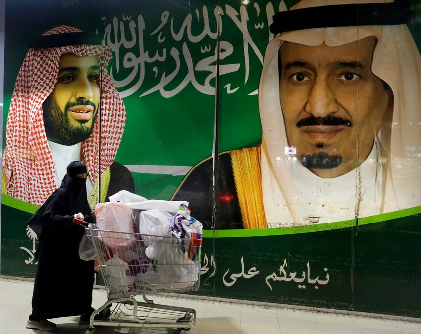 FILE - A Saudi woman pushes her shopping cart outside a supermarket in Jiddah, Saudi Arabia, on June 30, 2020, with Saudi King Salman, right, and Crown Prince Mohammed bin Salman depicted in a mural.