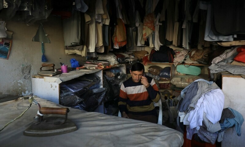 <p>A laundryman uses cell phone as he sits at his shop during country-wide power breakdown in Peshawar. — Reuters</p>