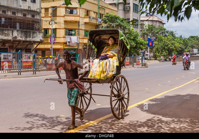 a-man-pulls-a-wooden-rickshaw-with-passenger-along-a-street-on-in-dhgf4b.jpg
