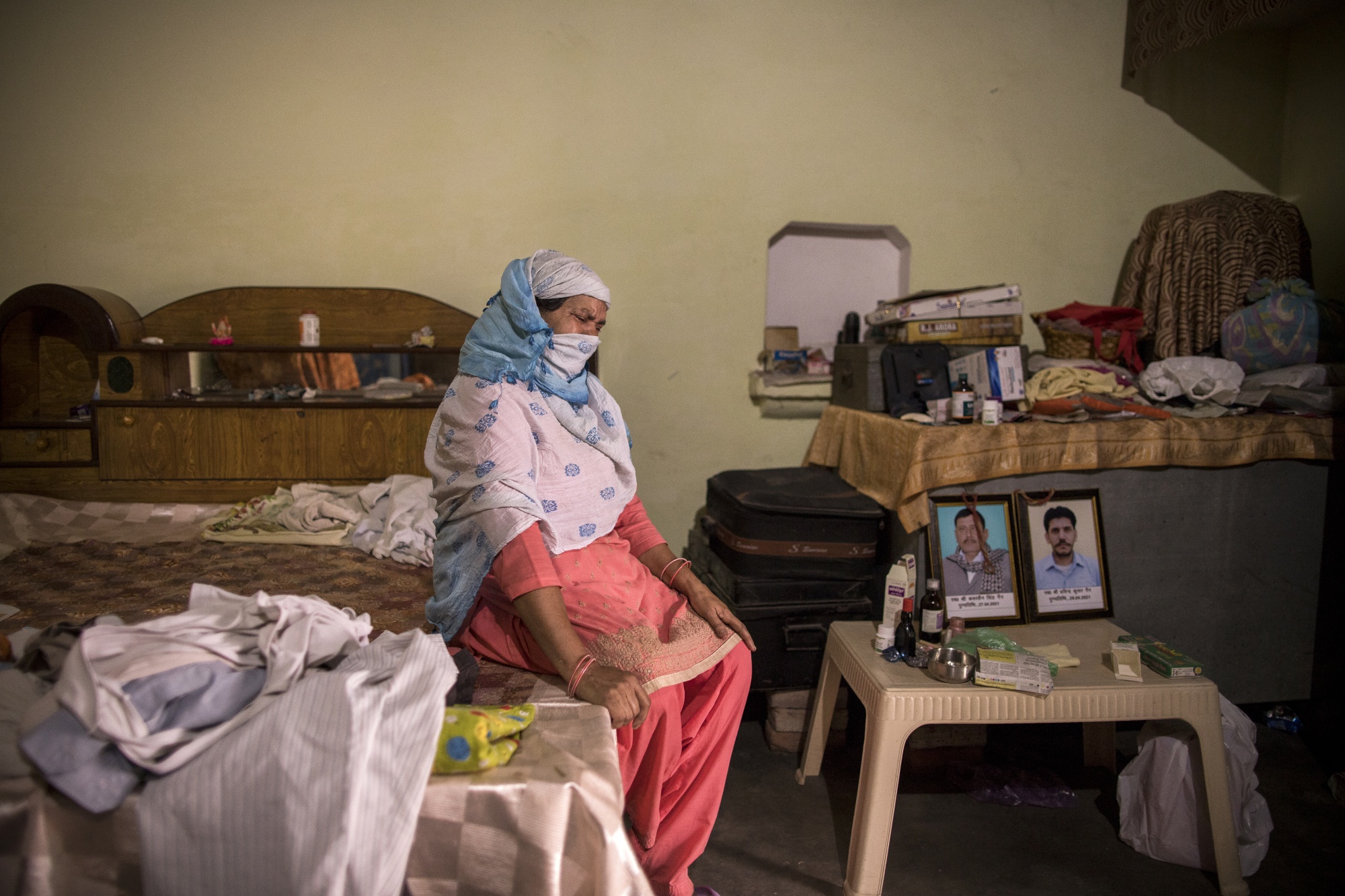 Wife of Covid fatality Kuwarsen Singh weeps next to portraits of diseased Kuwarsen Singh (L) and his son Pravinder Kumar. Kuwarsen singh was sent to an election duty where he was infected with the Covid virus. Picture taken at his house in the village Bassi, in Baghpath, Uttar Pradesh, India