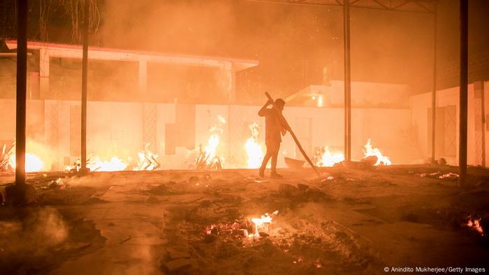 Workers can be seen at a crematorium where multiple funeral pyres are burning for patients who lost their lives to COVID