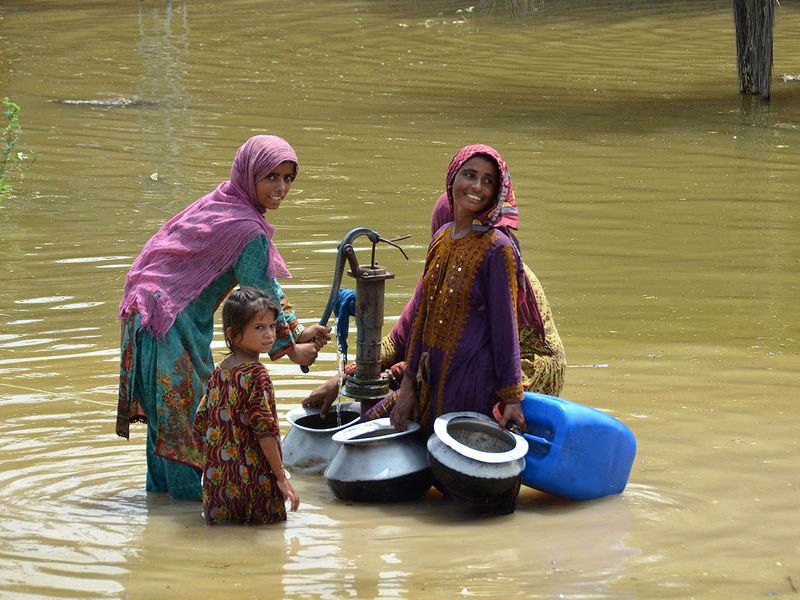 Flood affected women fill drinking water from a handpump amid a flooded street following heavy monsoon rains in Jaffarabad district of Balochistan province on August 29, 2022. - The death toll from monsoon flooding in Pakistan since June has reached 1,136, according to figures released on August 29 by the country's National Disaster Management Authority.