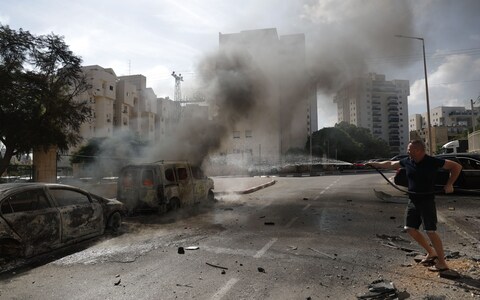 A resident douses burning vehicles in the Israeli city of Ashkelon following rocket launches from Gaza, 07 October 2023. 