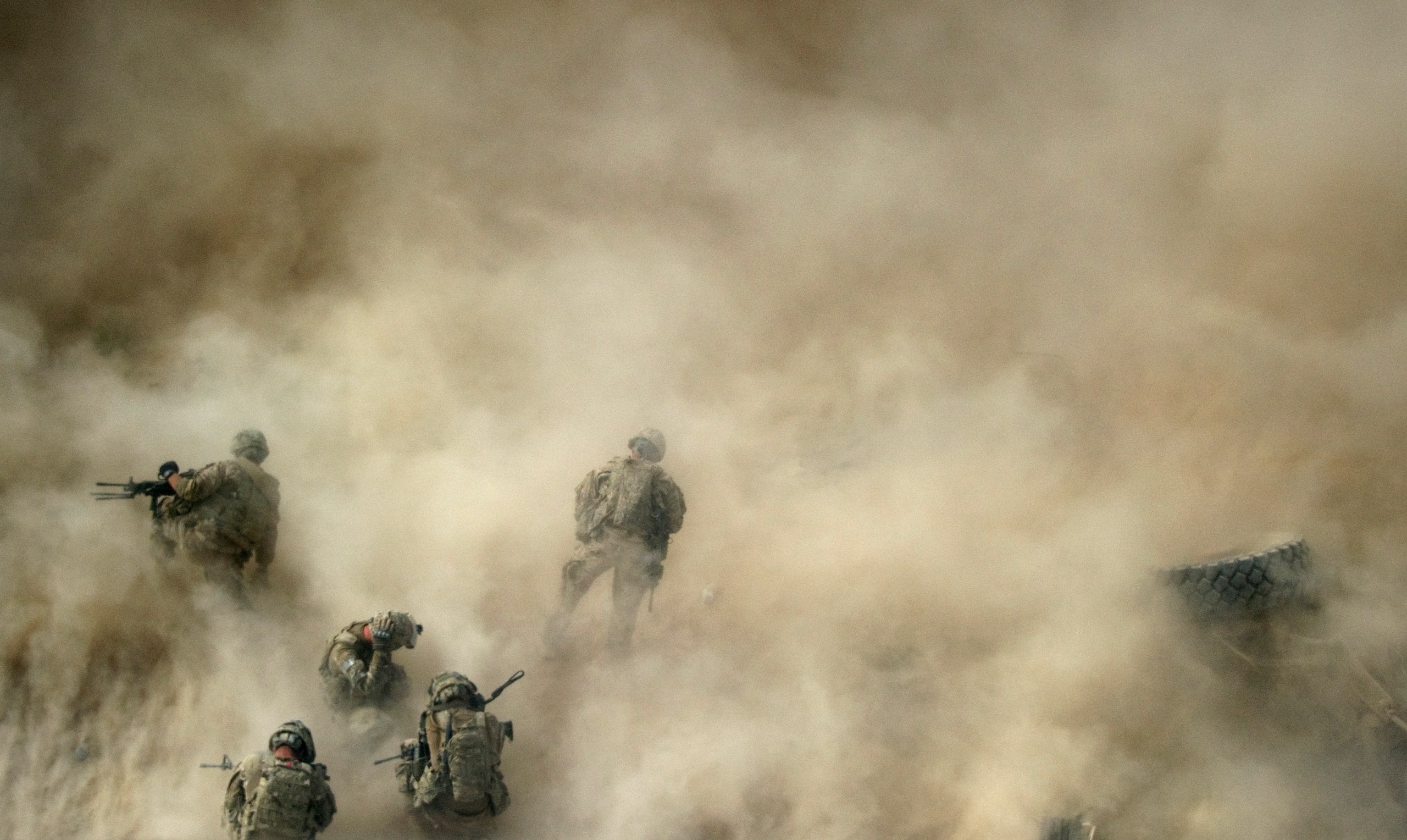 U.S. soldiers gather near a destroyed vehicle and protect their faces from rotor wash.