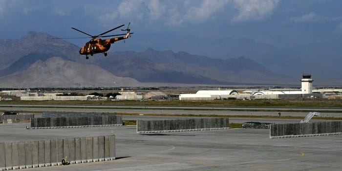 A dark-orange helicopter in the air above a sprawling air base.