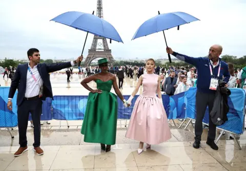  Christophe Petit-Tesson/PA Media Under umbrellas Ariana Grande hold hands with Cynthia Erivo as they arrive at the Trocadero