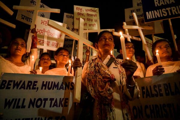 A crowd of women hold protest signs, white wooden crosses and tall white candles during a nighttime protest.