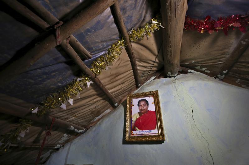 A portrait of Padmavathi, who died of COVID-19, hangs on the wall of her family hut made from bamboo and plastic sheeting  in a slum in Bengaluru, India, Thursday, May 20, 2021. Padmavathi collected hair, taking it from women's combs and hairbrushes to later be used for wigs. She earned about $50 a month. (AP Photo/Aijaz Rahi)