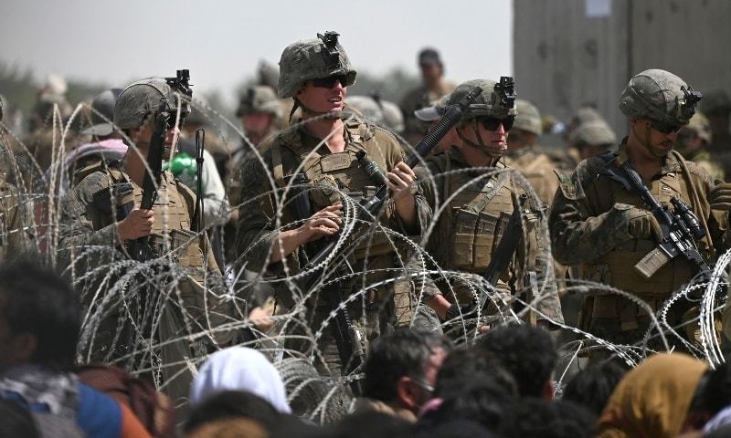 US soldiers stand guard behind barbed wire as Afghans sit on a roadside near the military part of the airport in Kabul on August 20. — AFP/File