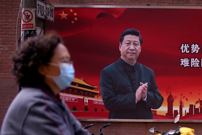 A woman wearing a protective mask is seen past a portrait of Chinese President Xi Jinping on a street as the country is hit by an outbreak of the coronavirus in Shanghai [File: Aly Song/ Reuters]