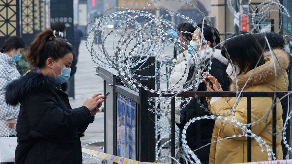 Xi'an residents stand by barbed wire topped gate on their mobiles