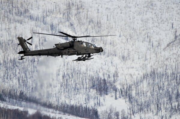 An Army helicopter flies over a snowy landscape in Alaska.