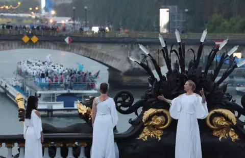  Pilar Olivares/Reuters Performers dressed in white robes stand on Pont Alexandre III during the opening ceremony of the Paris 2024 Olympics, as a boat passes beneath