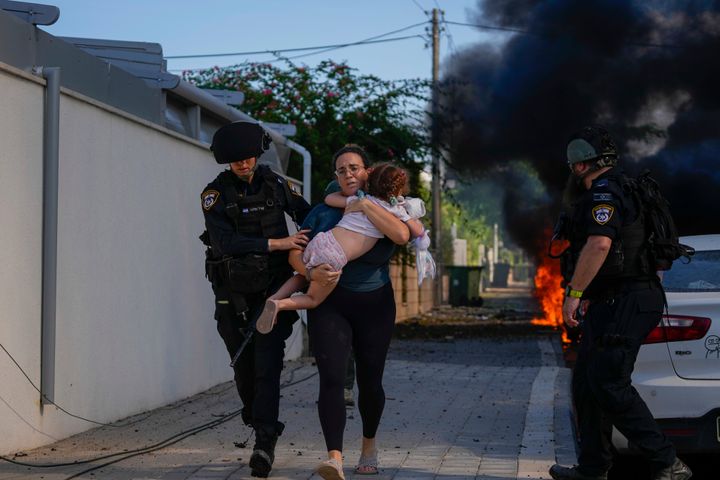 Israeli police officers evacuate a woman and a child from a site hit by a rocket fired from the Gaza Strip, in Ashkelon, southern Israel, Saturday, Oct. 7, 2023. The rockets were fired as Hamas announced a new operation against Israel. (AP Photo/Tsafrir Abayov)